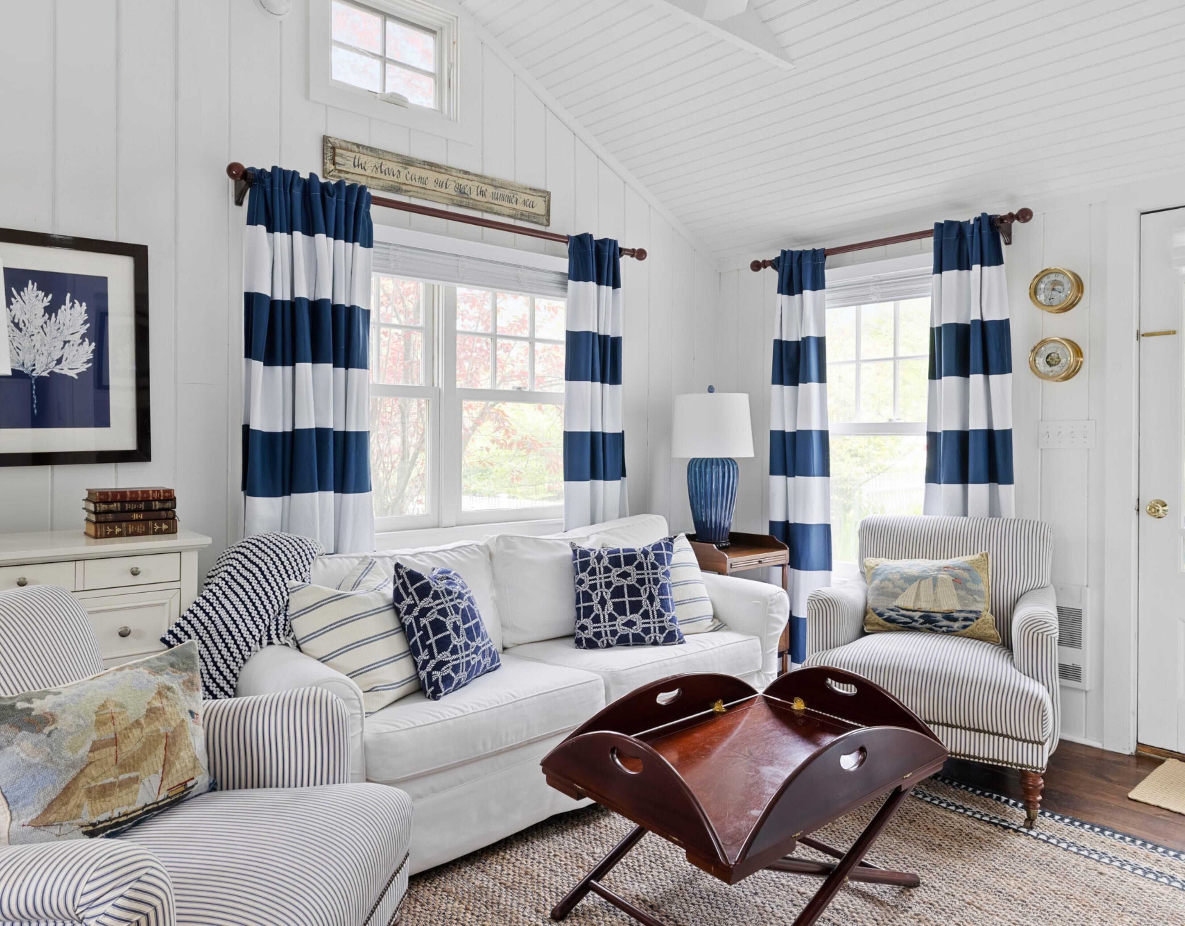 A room with a white sofa, striped armchairs, a wooden coffee table, and striped curtains.