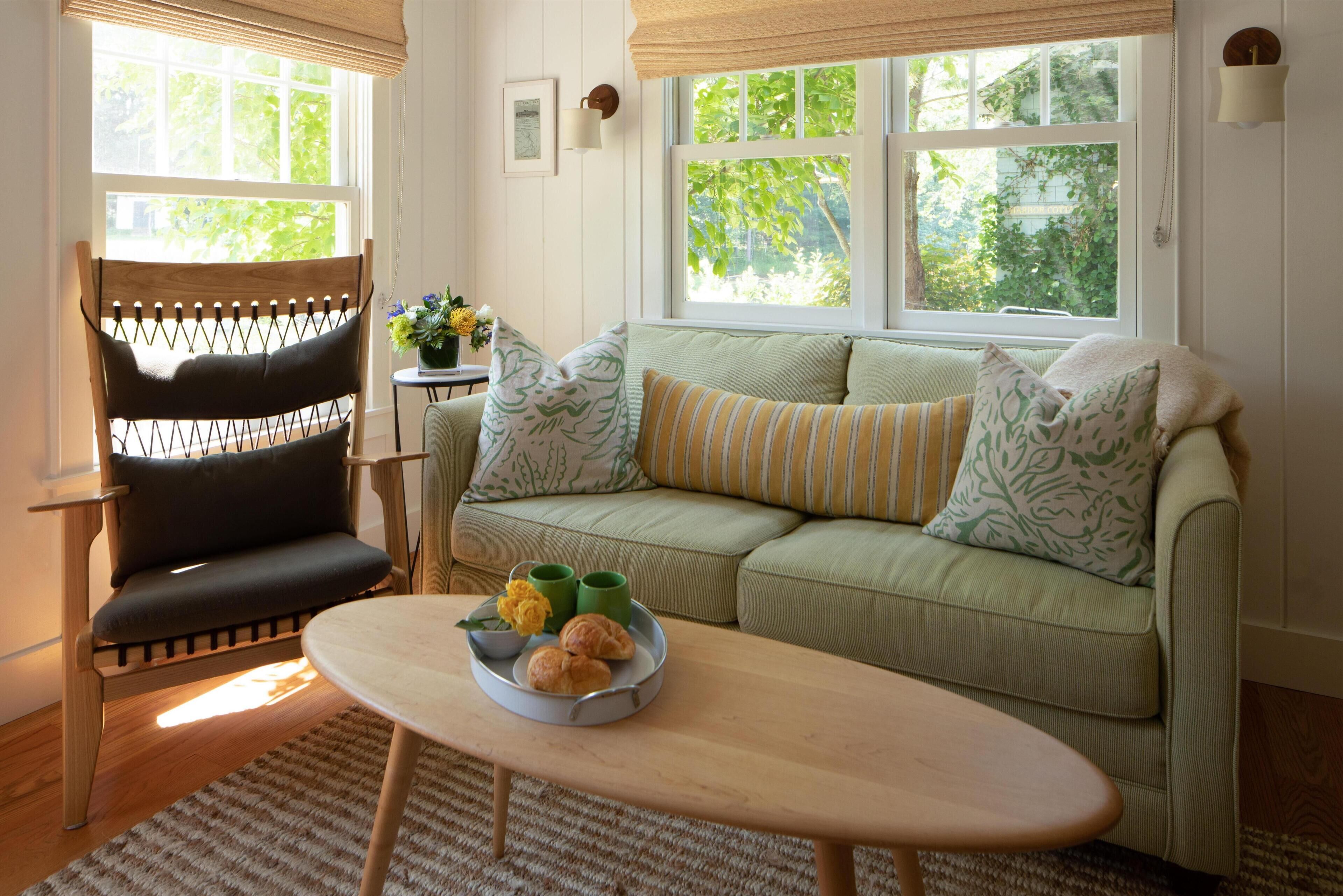 Un salon chaleureux avec un canapé vert, une chaise en bois et une table basse agrémentée d’un arrangement floral.