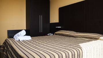 Habitación de hotel con una cama grande, un armario y una mesita de noche con un teléfono y una toalla doblada.