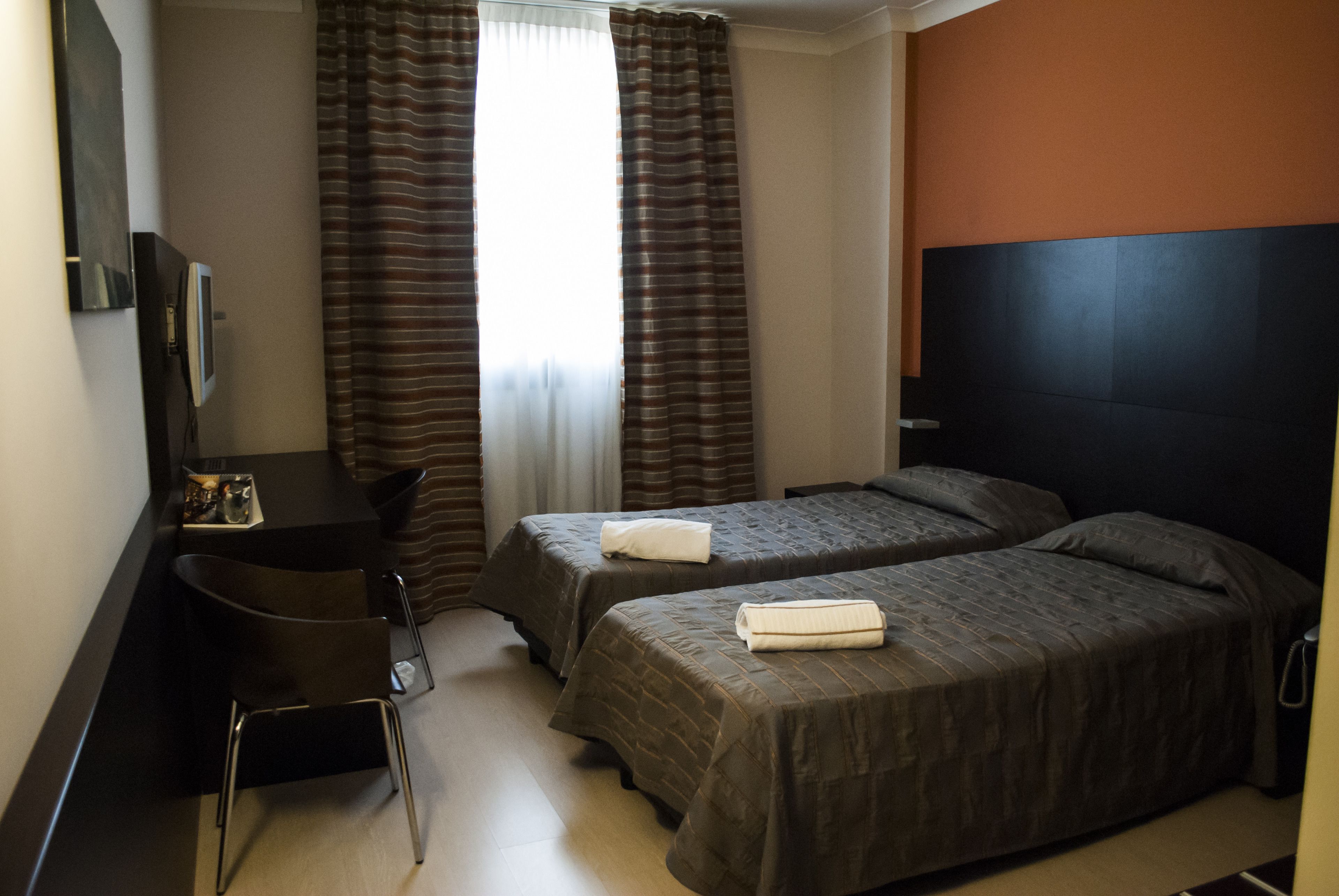 A hotel room with two beds, a desk, and a TV.