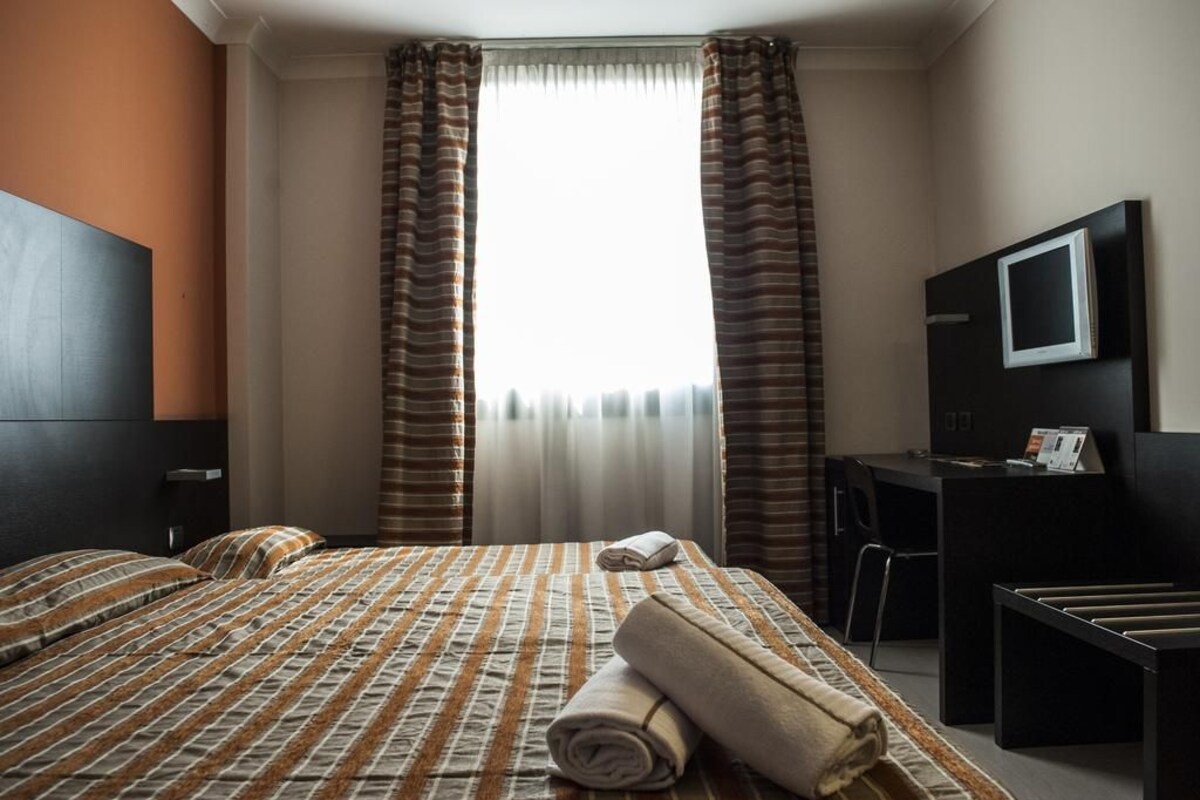 Una habitación de hotel con cama, escritorio, televisor y cortinas.
