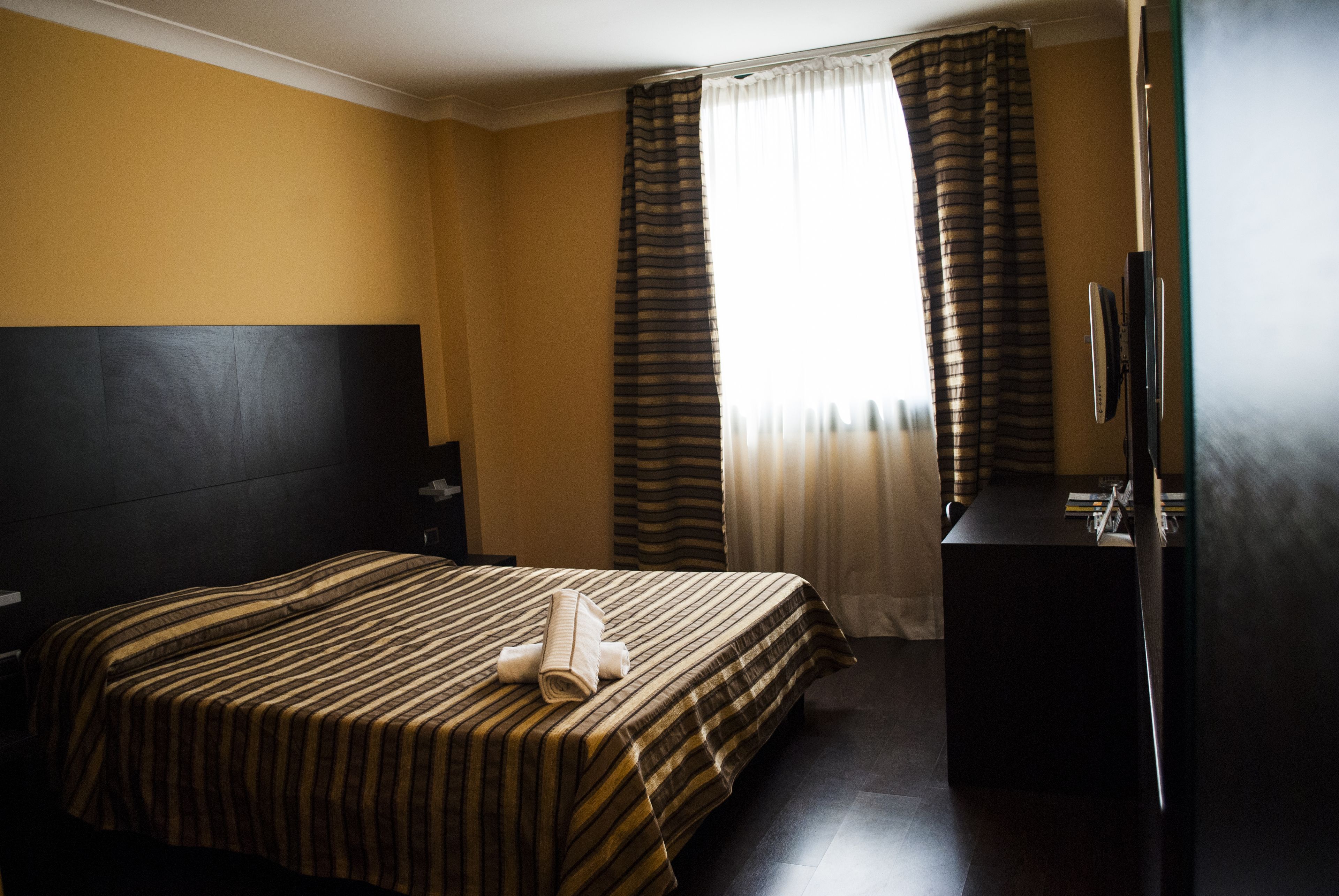 A hotel room with a bed, a desk, and a window with curtains.