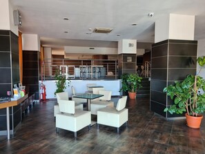 Un hall d’hôtel moderne comprenant un comptoir d’accueil, un espace salon et un escalier menant aux étages supérieurs.