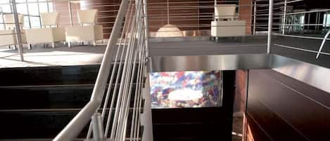 Un interior moderno con una escalera, una zona de estar y una gran pantalla que muestra arte abstracto.