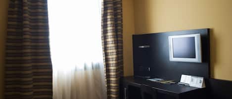 A hotel room with a bed, a desk with a computer, a TV, and curtains.