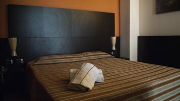 A hotel room with a large bed, striped bedding, a dark headboard, bedside lamps, and a painting on the wall.