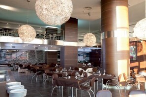 Un restaurante moderno con mesas y sillas redondas, grandes lámparas esféricas colgantes y una escalera que conduce a un nivel superior.