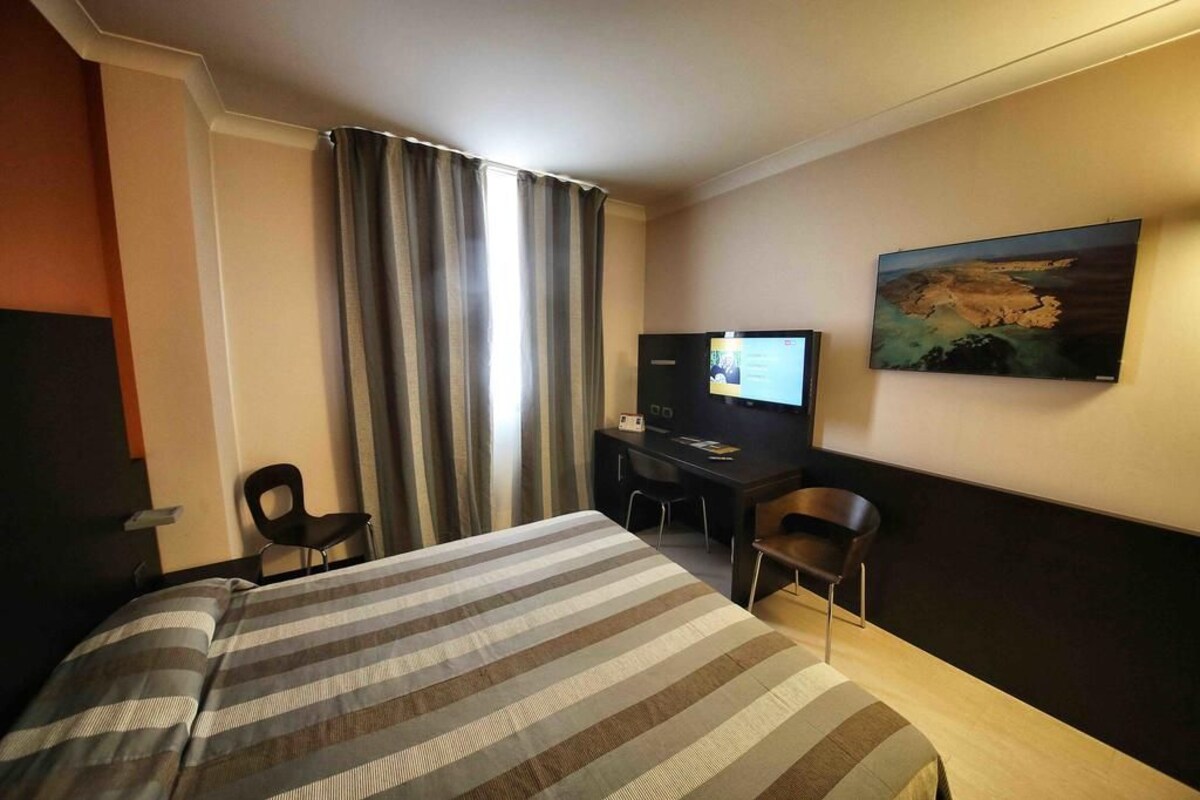 Habitación de hotel con cama, escritorio, televisor y un cuadro en la pared.