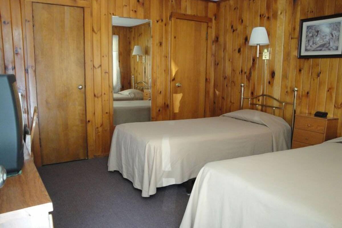 A room with two beds, wooden walls, a desk, a mirror, and a framed picture on the wall.