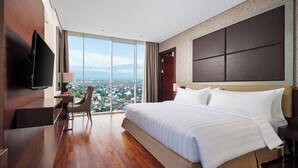 Ein modernes Hotelzimmer mit einem großen Bett, einem Schreibtisch, einem Sessel, einem Fernseher und Blick auf die Stadt.