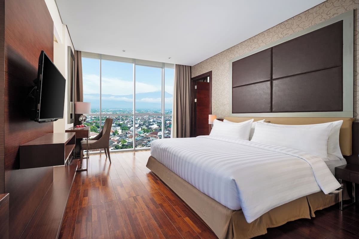 Een moderne hotelkamer met een groot bed, een bureau, een stoel, een televisie en uitzicht op de stad.