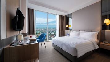 Une chambre d’hôtel avec un grand lit, un bureau avec une chaise, un téléviseur fixé au mur et une vue sur la ville.