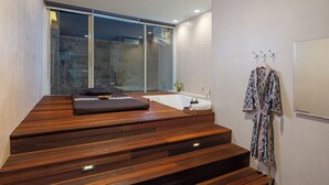 Ein moderner Spa-Raum mit einer Holzbank, einer großzügigen Badewanne und einer Glaswand mit Blick auf eine Steinwand.