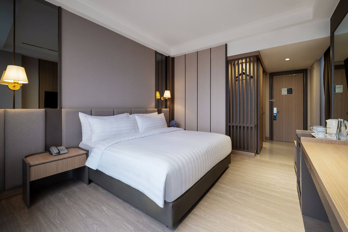 Een moderne hotelkamer met een groot bed, een nachtkastje met een telefoon, een bureau met een koffiezetapparaat en een spiegel.