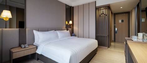 A modern hotel room with a large bed, a bedside table with a phone, a desk with a coffee maker, and a mirror.