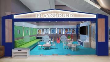 Explore the ASTON playground, featuring a green seating area, tables, chairs, and a variety of play structures.