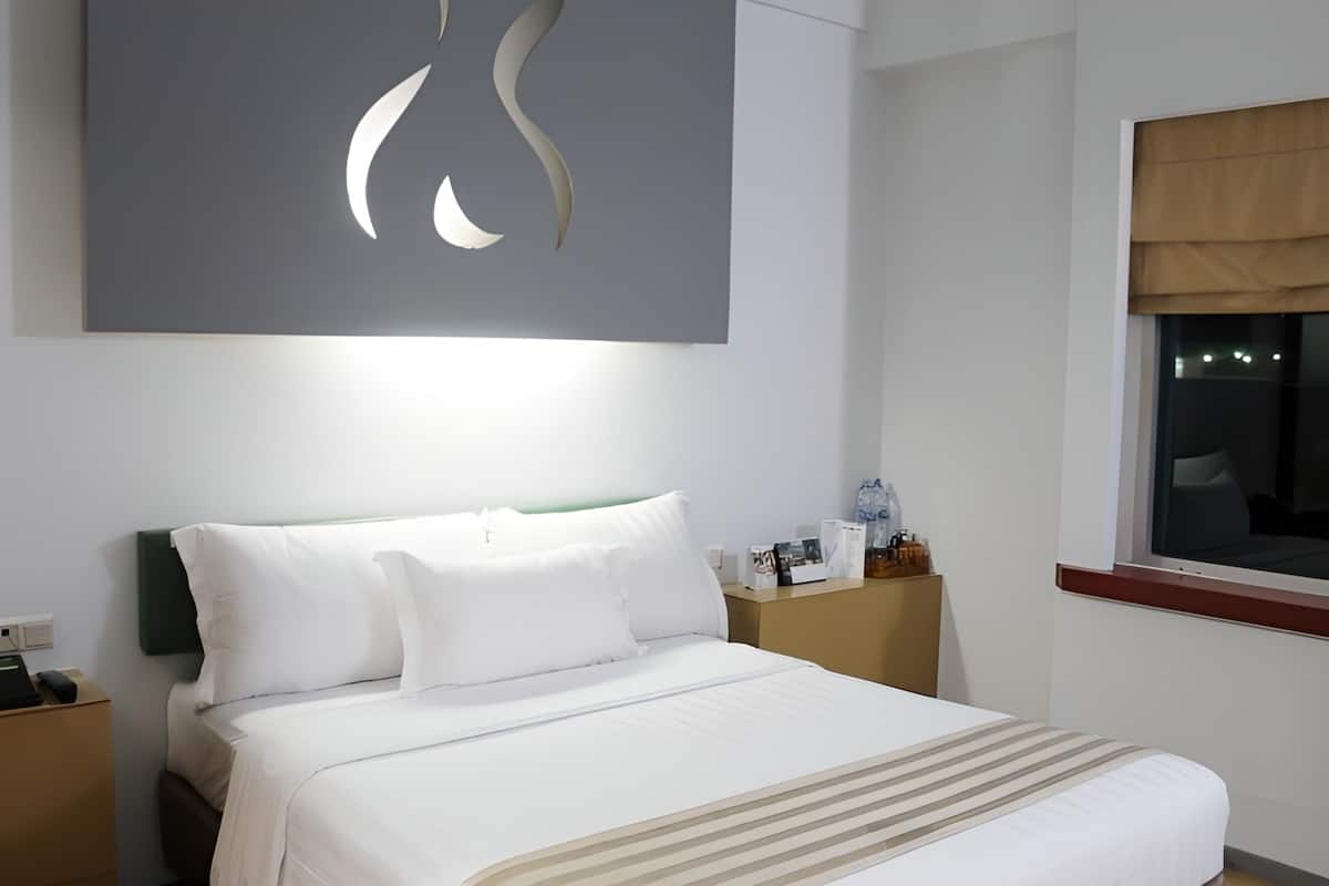 Une chambre d’hôtel avec un lit bien fait, une table de chevet avec une lampe, une fenêtre donnant sur un beau paysage et une œuvre d’art accrochée au mur.