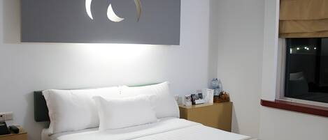 Una habitación de hotel con una cama bien hecha, una mesita de noche con una lámpara, una ventana con vistas y una obra de arte en la pared.