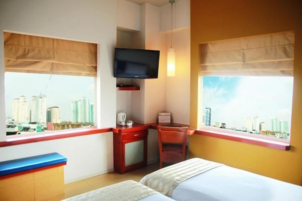 A hotel room with a bed, a desk, a chair, a television, and a window with a city view.