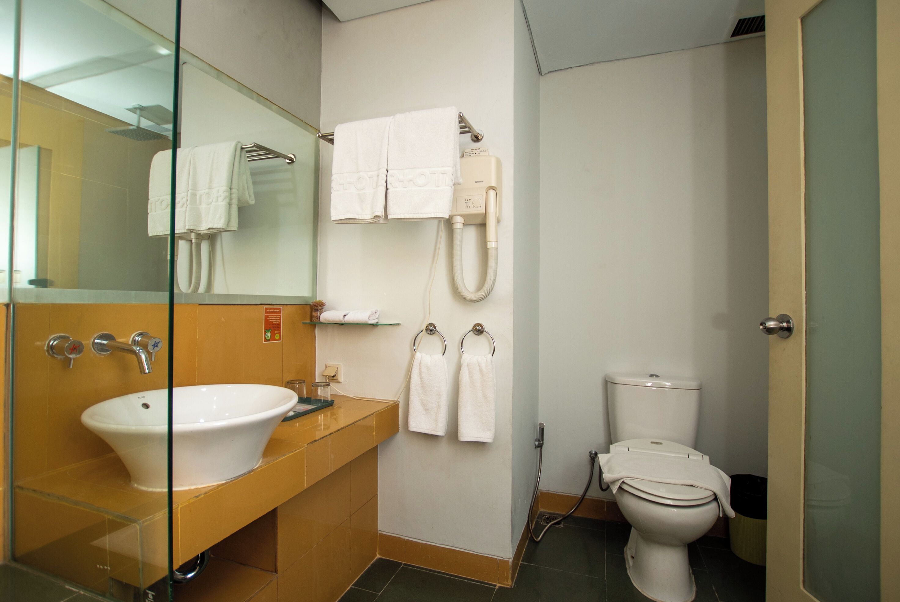 Un baño con lavamanos con cristal, inodoro y zona de ducha.