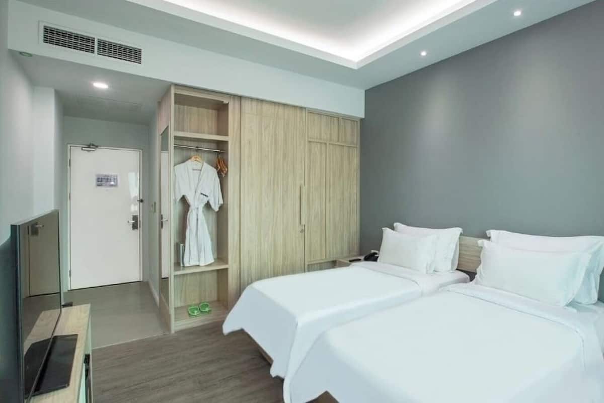 Une chambre d’hôtel moderne avec deux lits, une armoire et une petite table sur laquelle est posée une orchidée en pot.