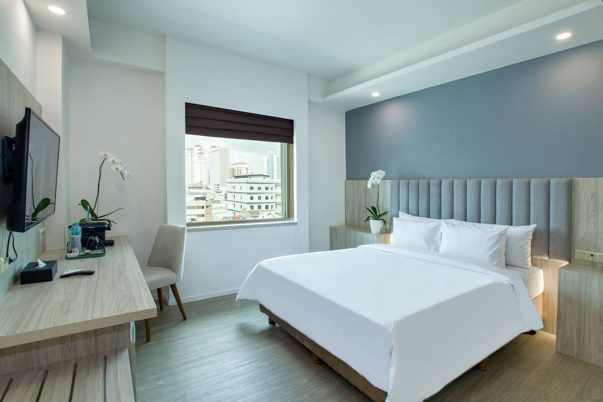 Une chambre d’hôtel moderne dotée d’un grand lit, d’un bureau avec une chaise, d’une télévision et d’une fenêtre donnant sur la ville.