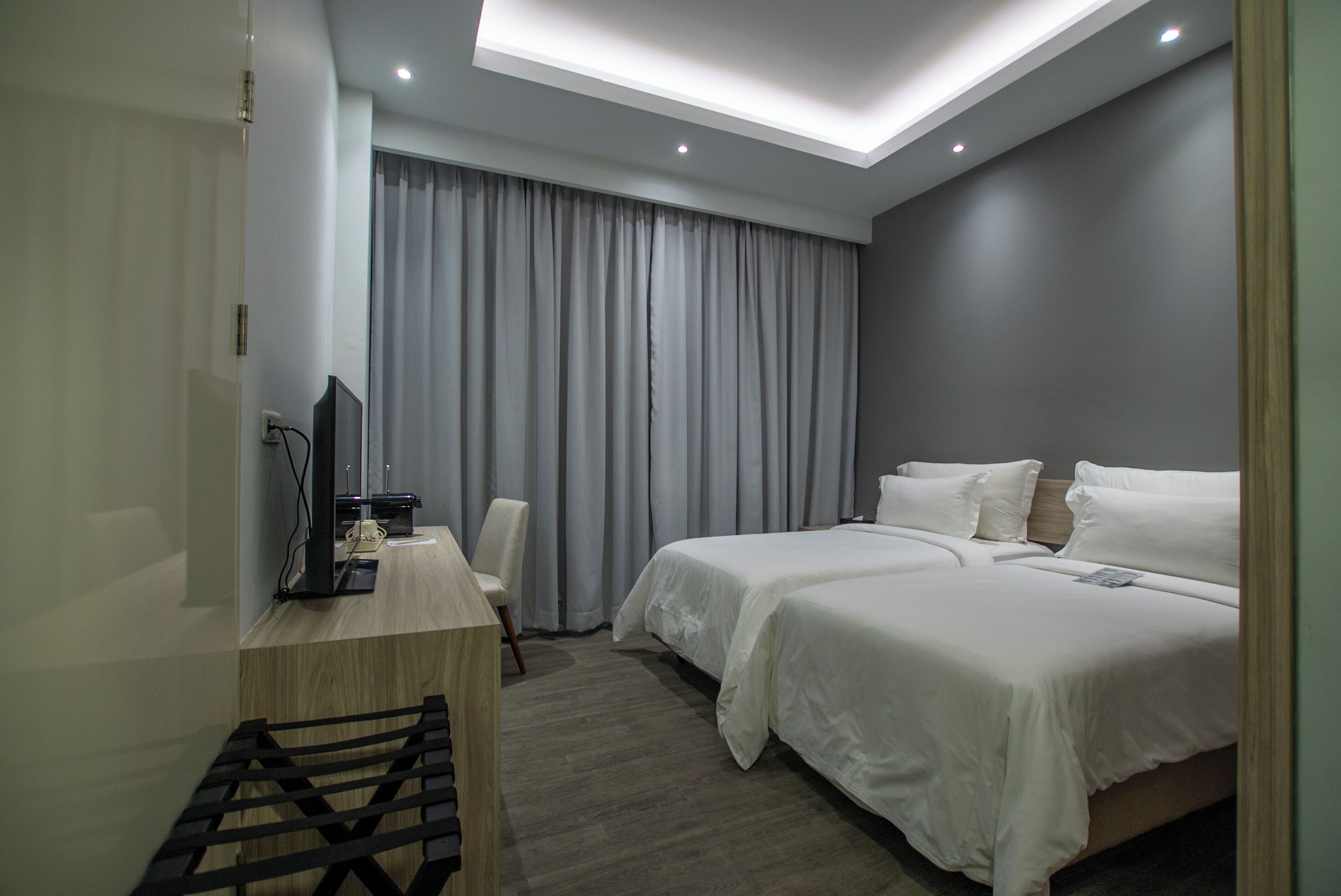 Une chambre d’hôtel moderne équipée d’un lit, d’un bureau avec un ordinateur et d’une grande fenêtre avec des rideaux.