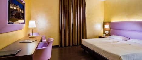 A hotel room with a bed, desk, chair, and a TV mounted on the wall.