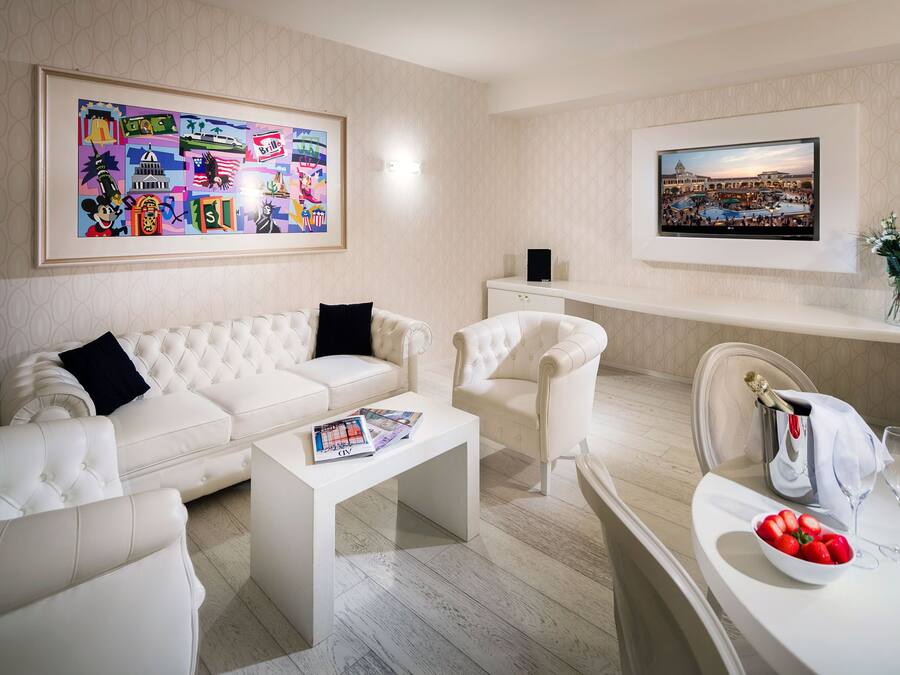 A modern living room with a white sofa, a coffee table, and a TV mounted on the wall. There is a framed picture above the sofa and another on the wall to the right.