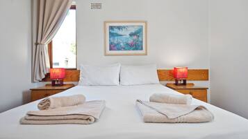 Een net opgemaakt bed met twee kussens, een schilderij aan de muur en twee bedlampjes.