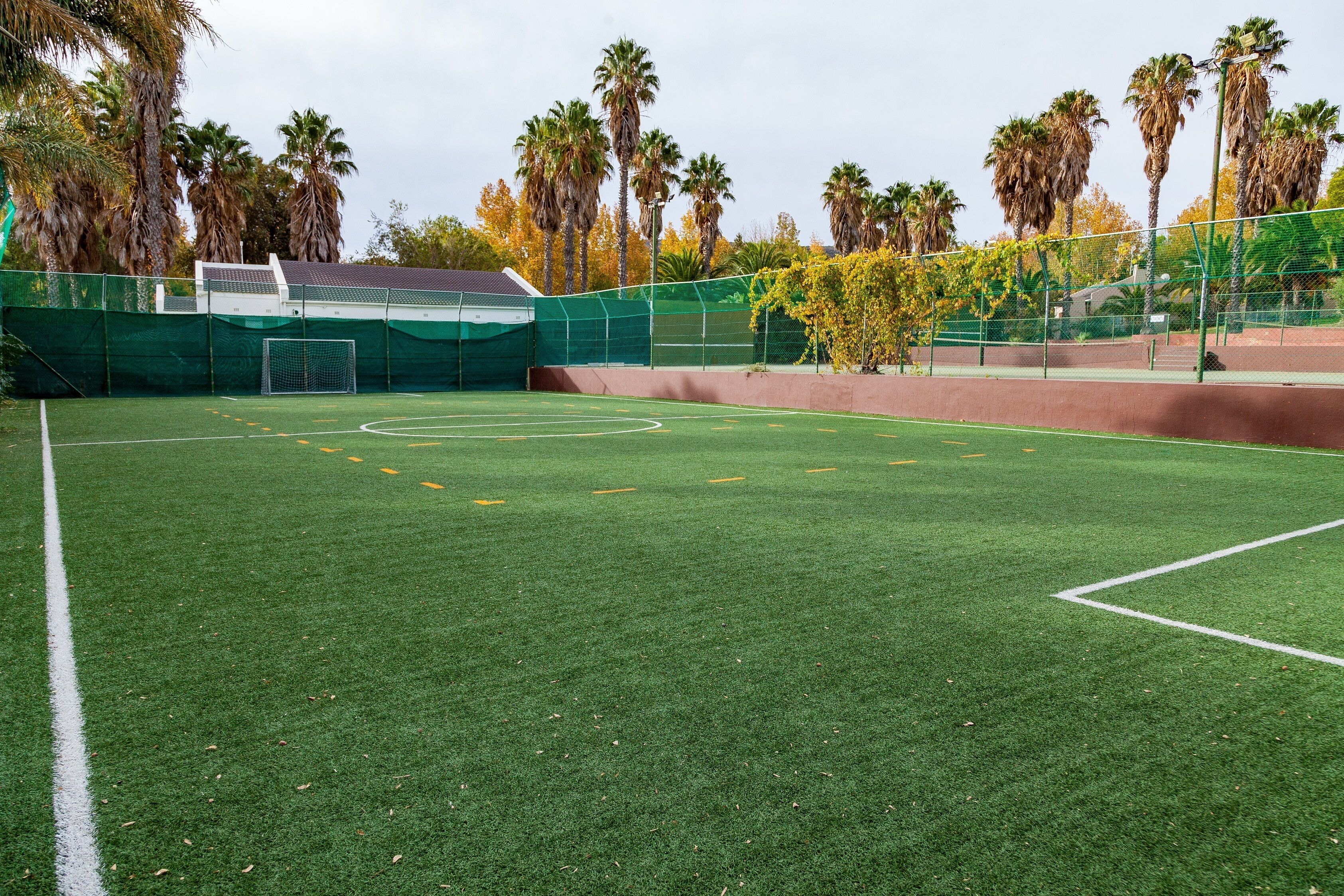 A sports field with green artificial turf, goalposts, and a fence.