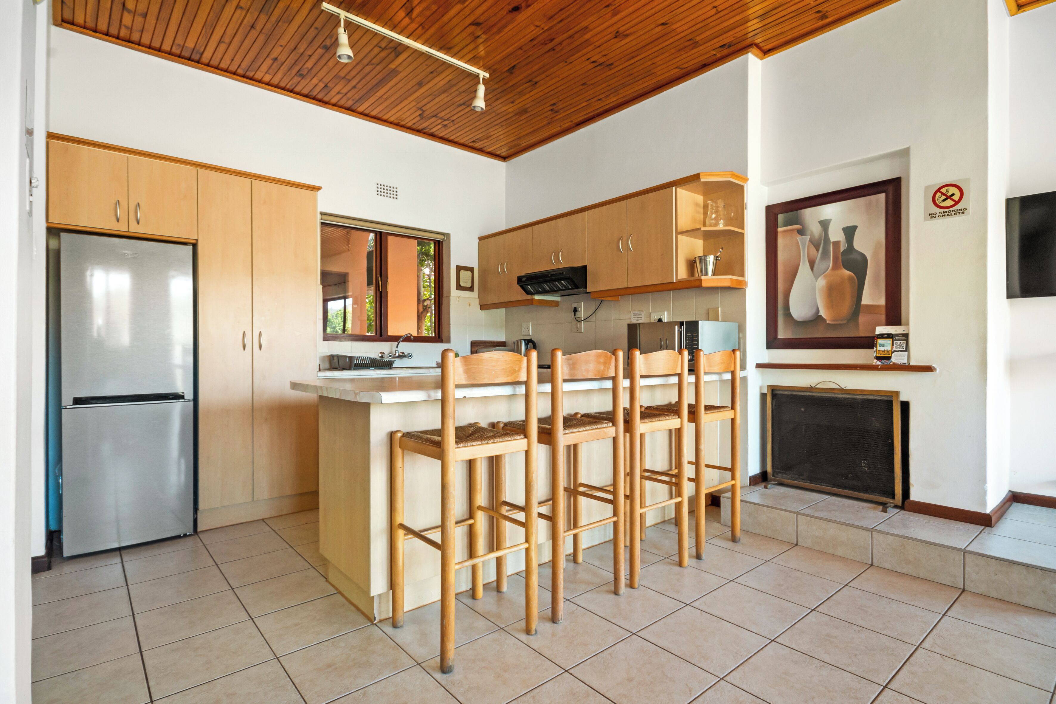 Una cocina moderna con armarios de madera, un refrigerador de acero inoxidable, una barra con taburetes y un suelo de baldosas.