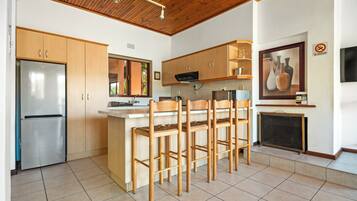 Una cocina moderna con armarios de madera, un refrigerador de acero inoxidable, una barra con taburetes y un suelo de baldosas.