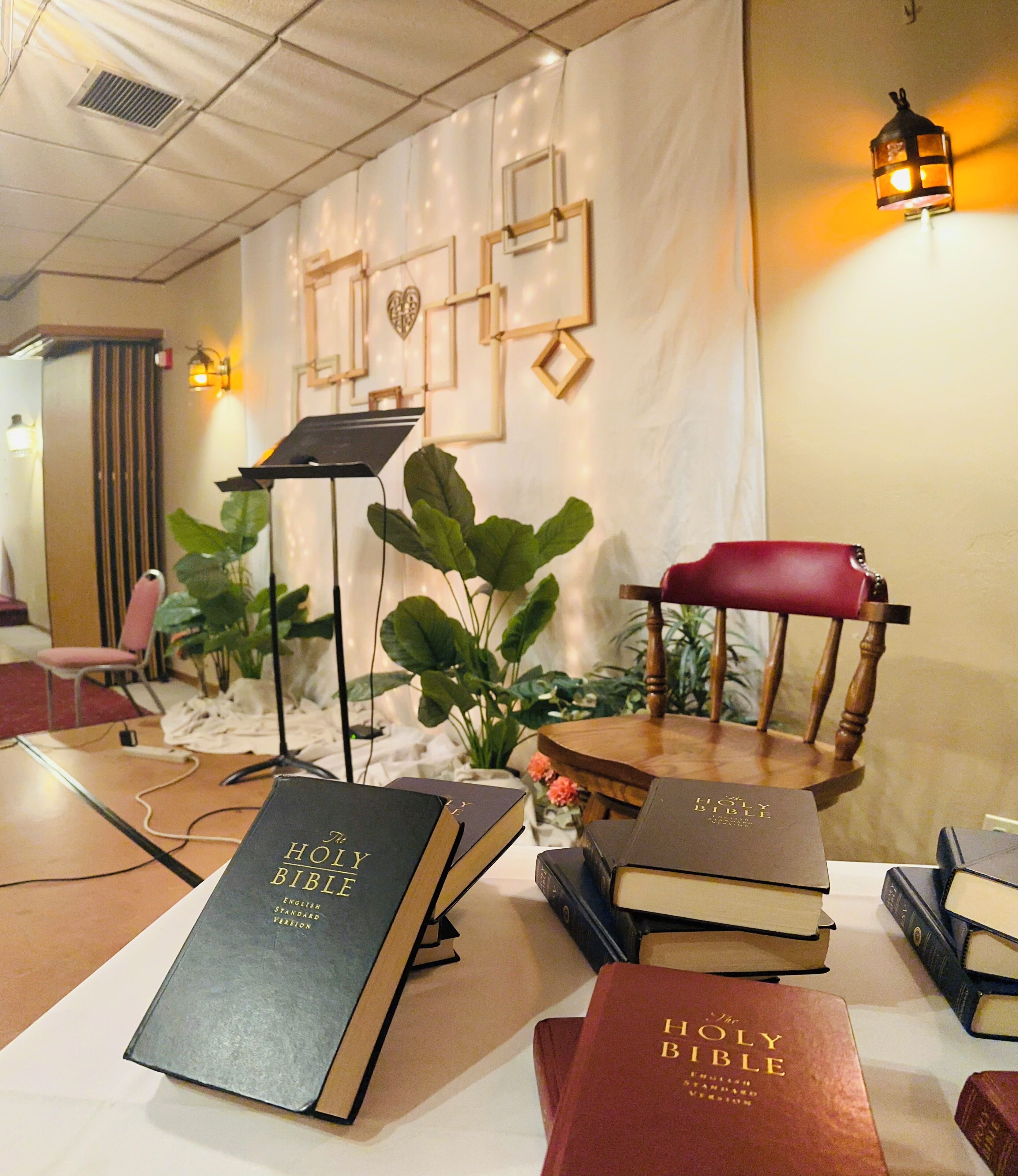 Une pièce comprenant une table où sont exposés plusieurs exemplaires de la Bible, un pied de micro et une chaise.