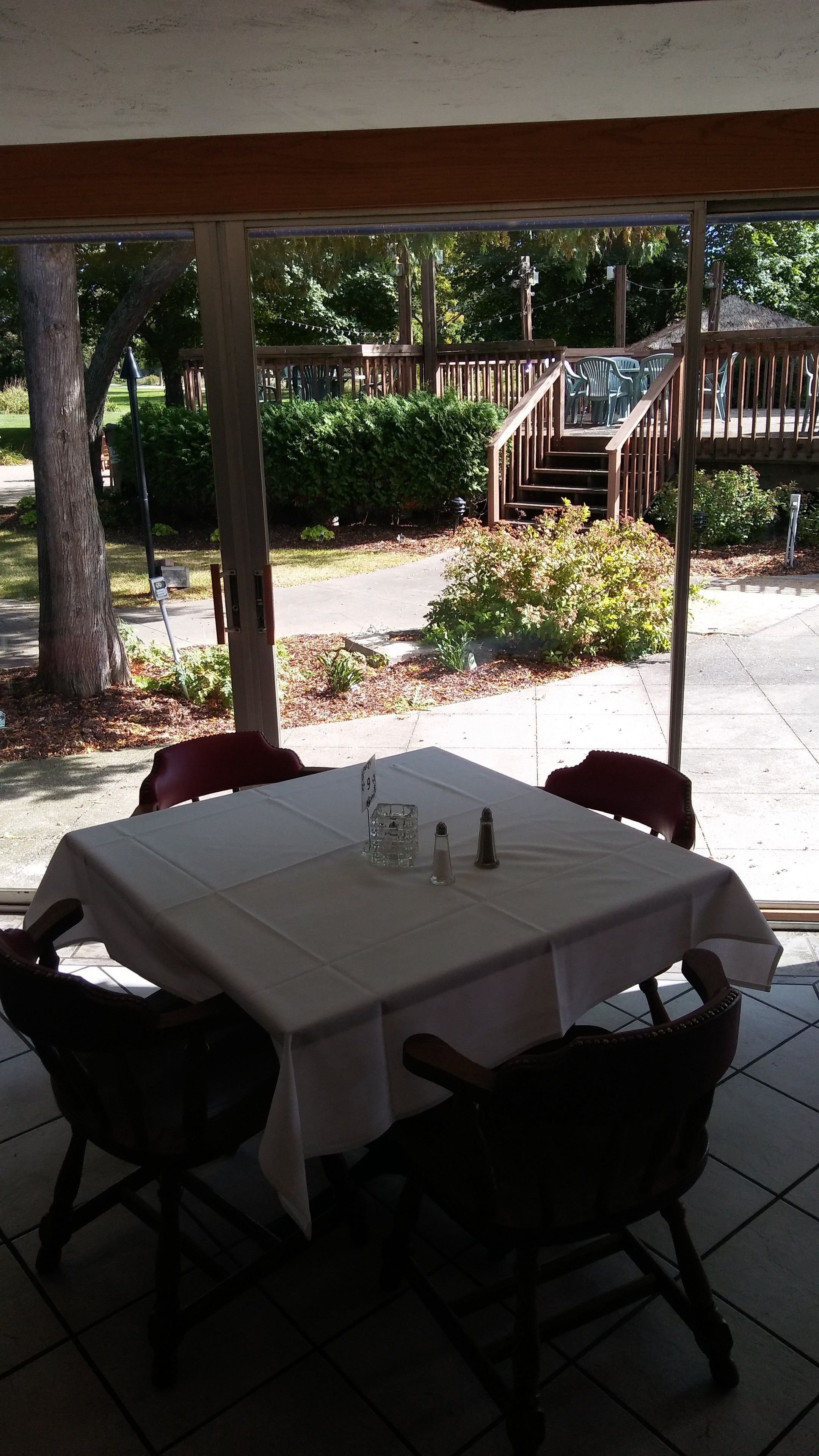 Een terras buiten, met een tafel gedekt voor twee personen, omringd door stoelen en uitzicht op een tuin en een houten terras.