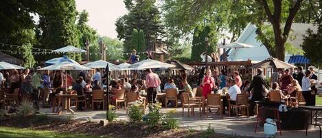An outdoor dining area with tables and chairs, surrounded by trees and covered by umbrellas.