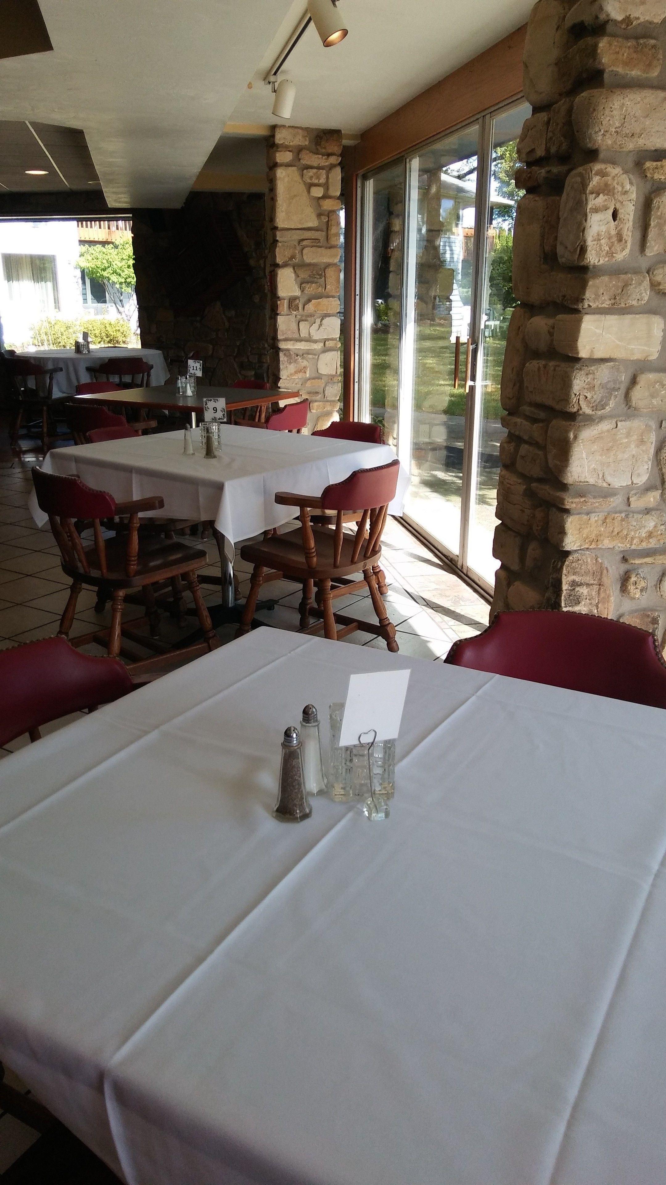 A restaurant with stone walls, large windows, and tables set for dining.