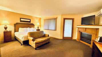A hotel room with a bed, a leather armchair, a television, a fireplace, and a door with a window.