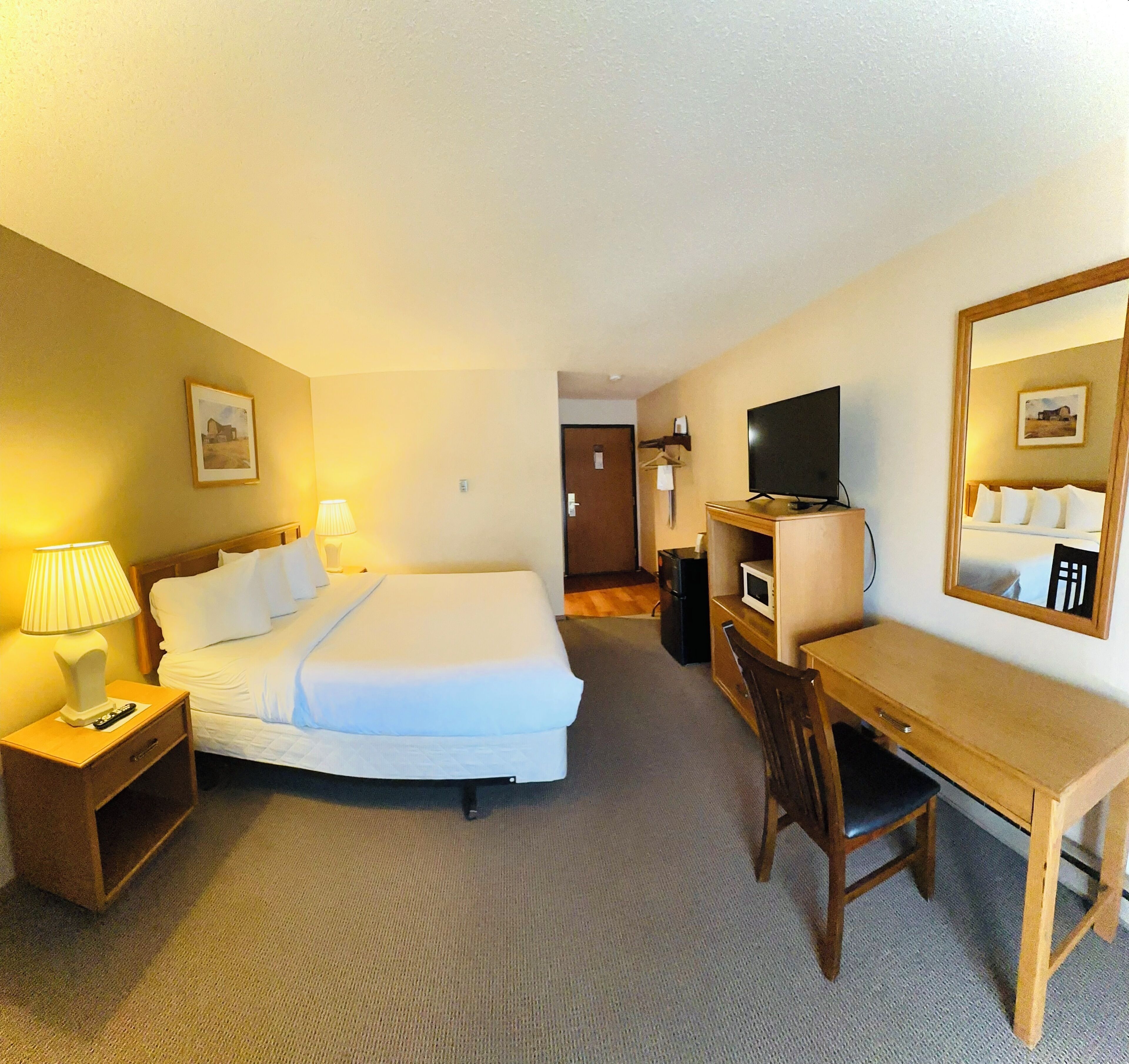 A hotel room with a bed, bedside tables, a desk, a chair, a television, and a mirror.