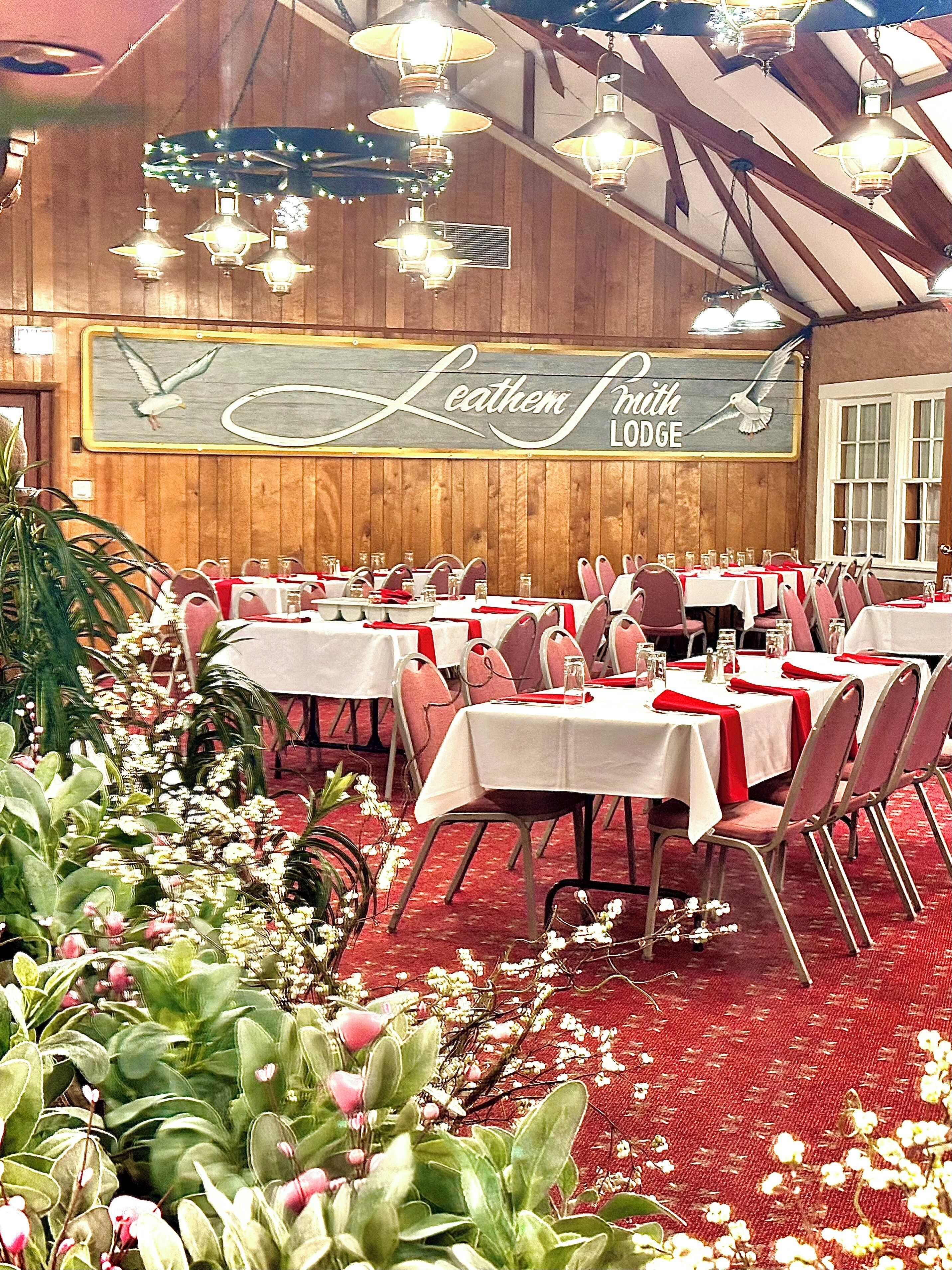 Ein Restaurantinneres mit mehreren Tischen, roten Stühlen und einer Holzwand mit dem Schild 'Leather Smith Lodge'.