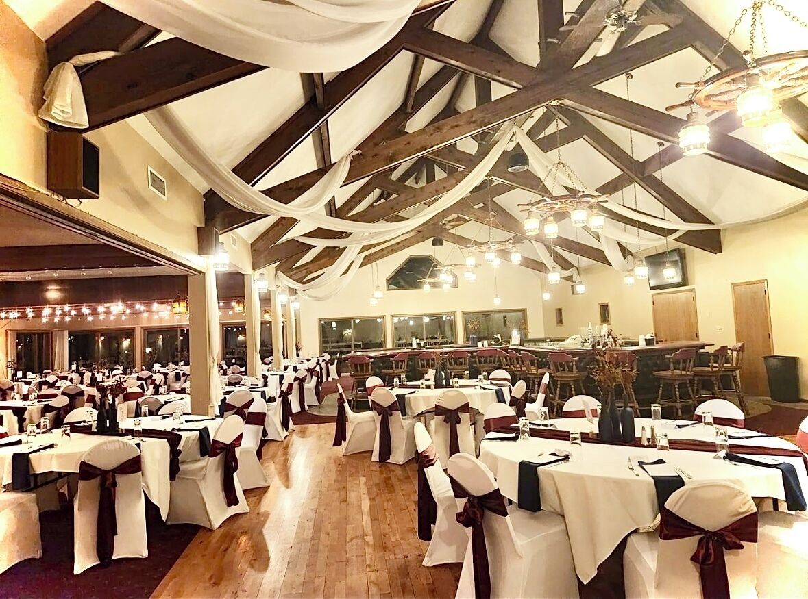 A banquet hall with tables set for a formal event, featuring exposed wooden beams and chandeliers.