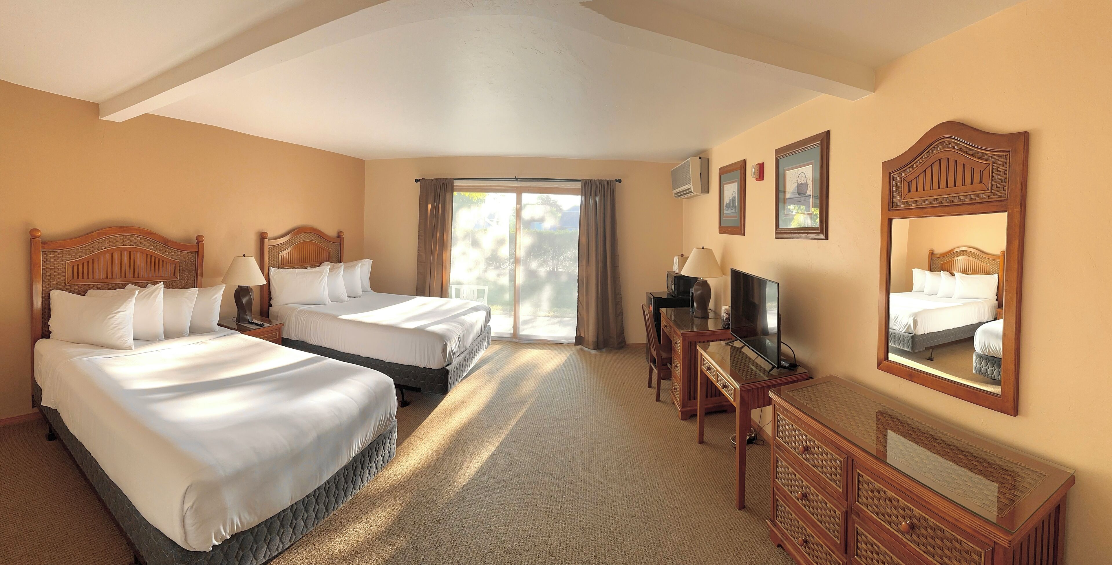 A hotel room with two beds, a desk, a TV, and a large window with curtains.