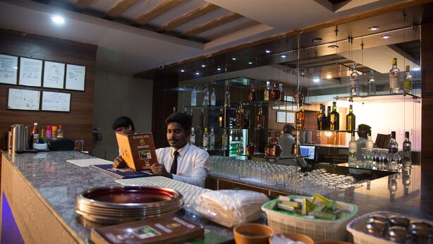 A bar area with a counter, glasses, and bottles. There are menus and a computer on the counter. - Mahalaya Residency (Chennai)