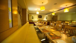 A restaurant with long communal tables, wooden chairs, and yellow pendant lights. - Mahalaya Residency (Chennai)