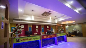A reception desk with a clock, a computer, and a flower arrangement. - Mahalaya Residency (Chennai)