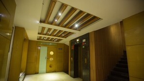 A hotel lobby with a wooden staircase, a reception desk, and a door with a circular window. - Mahalaya Residency (Chennai)