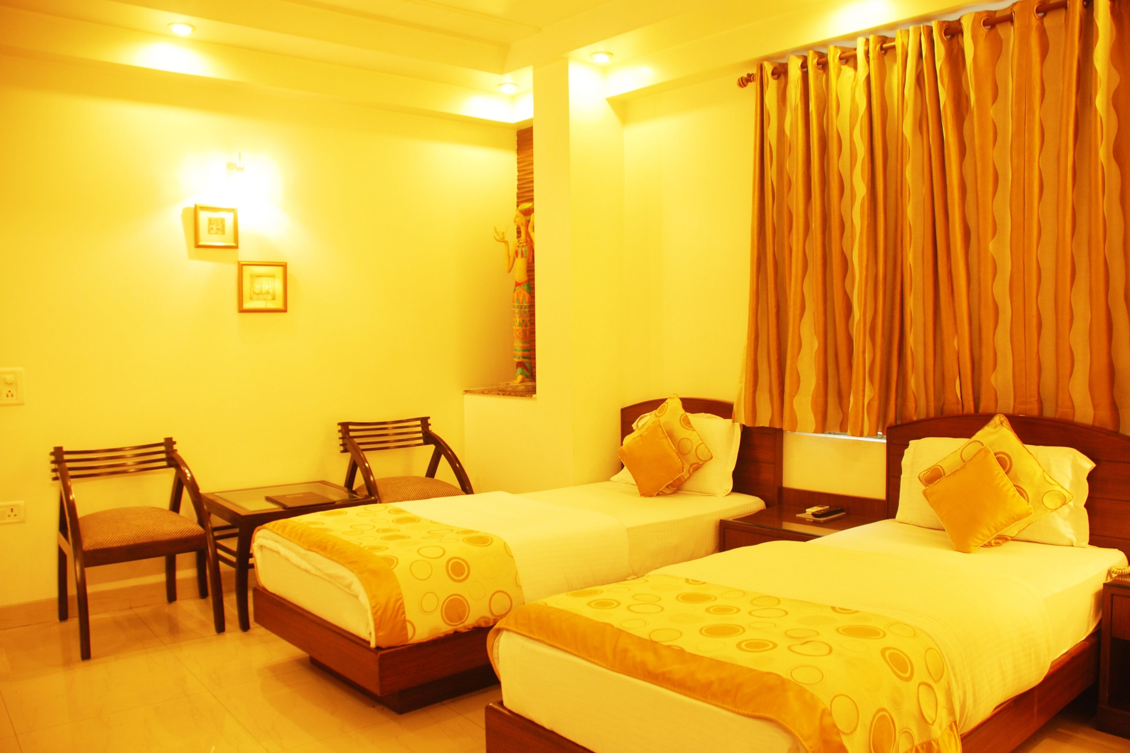 A hotel room with two single beds, a small table, two chairs, and a nightstand with a lamp.