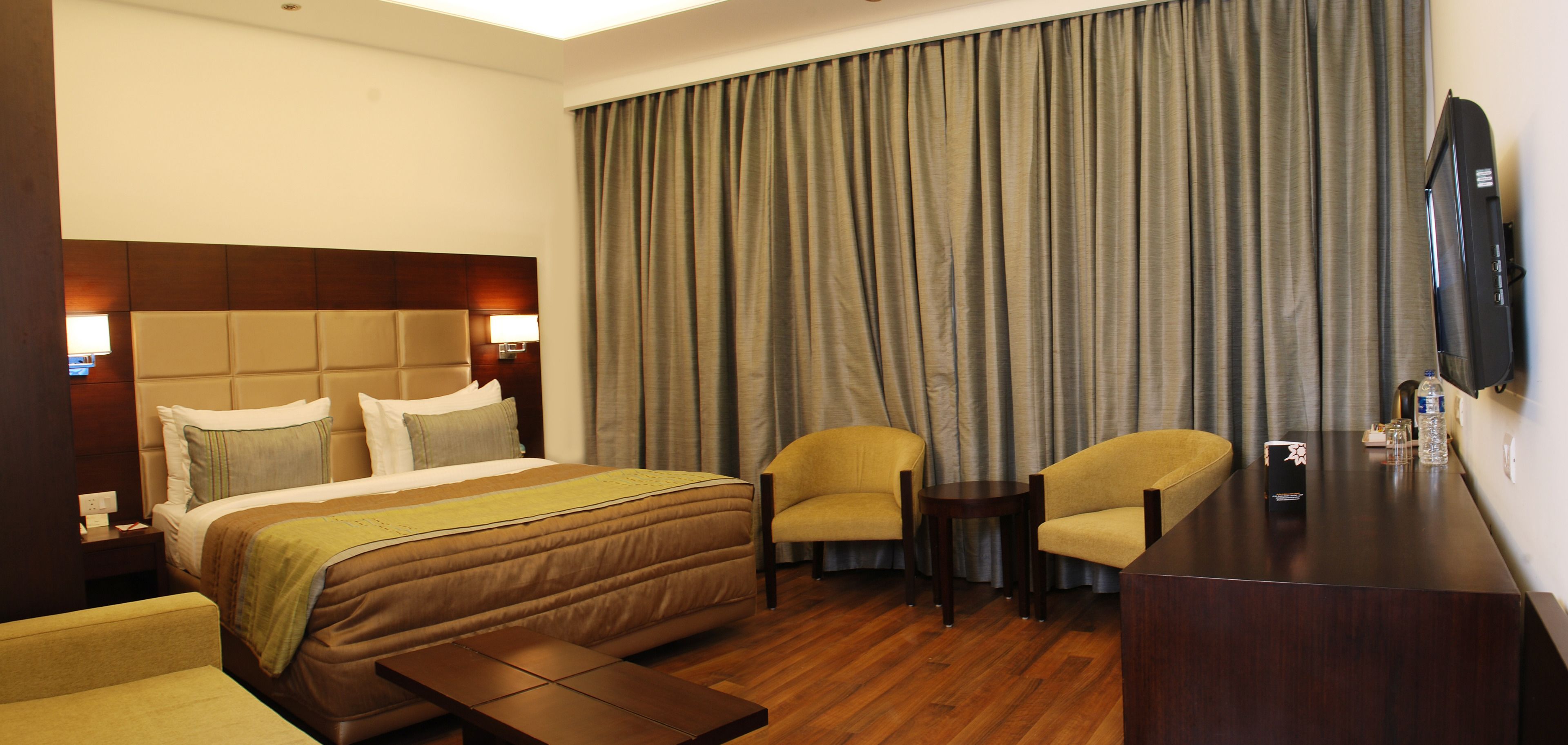 A hotel room with a large bed, two armchairs, a small table, a TV, and a curtain.
