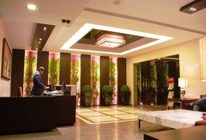 A hotel lobby with a reception desk, a seating area, and a large mirror. - Hotel Africa Avenue G K 1 (New Delhi)