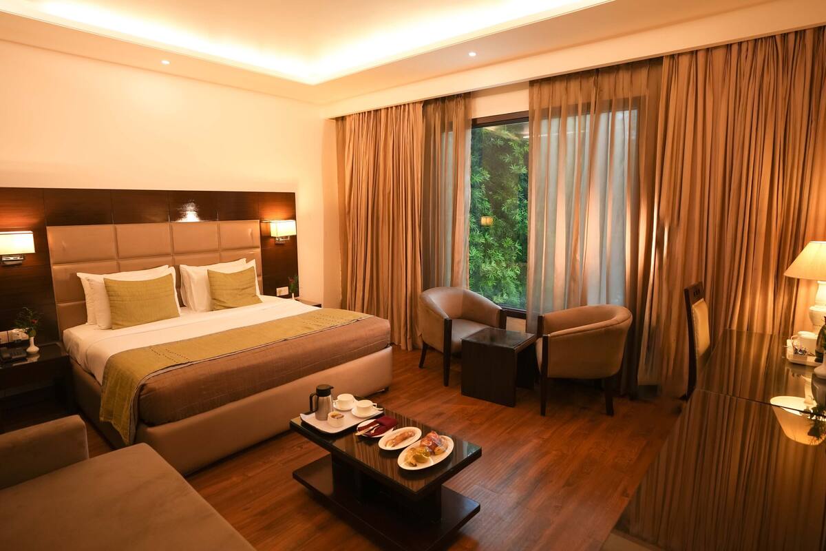 Une chambre d’hôtel avec un grand lit, un coin salon avec une table et une vue sur la verdure.